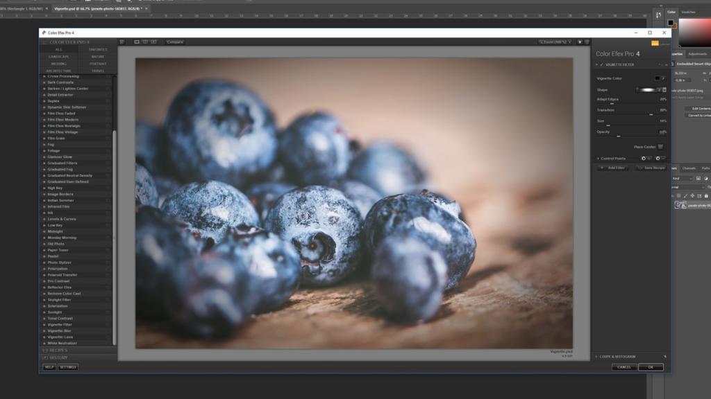 Primo piano di mirtilli su una superficie di legno, visualizzati sullo schermo di un computer all'interno di un'interfaccia software di fotoritocco. I pannelli e gli strumenti del software, tra cui la vignettatura in Photoshop, sono visibili attorno all'immagine. I mirtilli sono a fuoco, evidenziandone la consistenza e il colore.