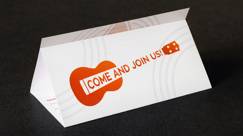 Una carta piegata su una superficie scura presenta una grafica di chitarra arancione con le parole COME AND JOIN US! creativamente integrate nel corpo della chitarra, riecheggiando il design di un pieghevole a sei pagine. La carta è in piedi in stile tenda.