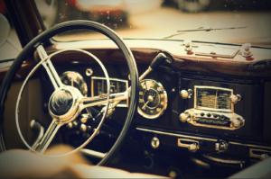 Primo piano del cruscotto di un'auto d'epoca, migliorato con un effetto vignettatura in Photoshop, con un grande volante con centro cromato, un tachimetro analogico, una radio vecchio stile con pulsanti e pannelli in legno lucidato. L'aspetto generale è classico e retrò.