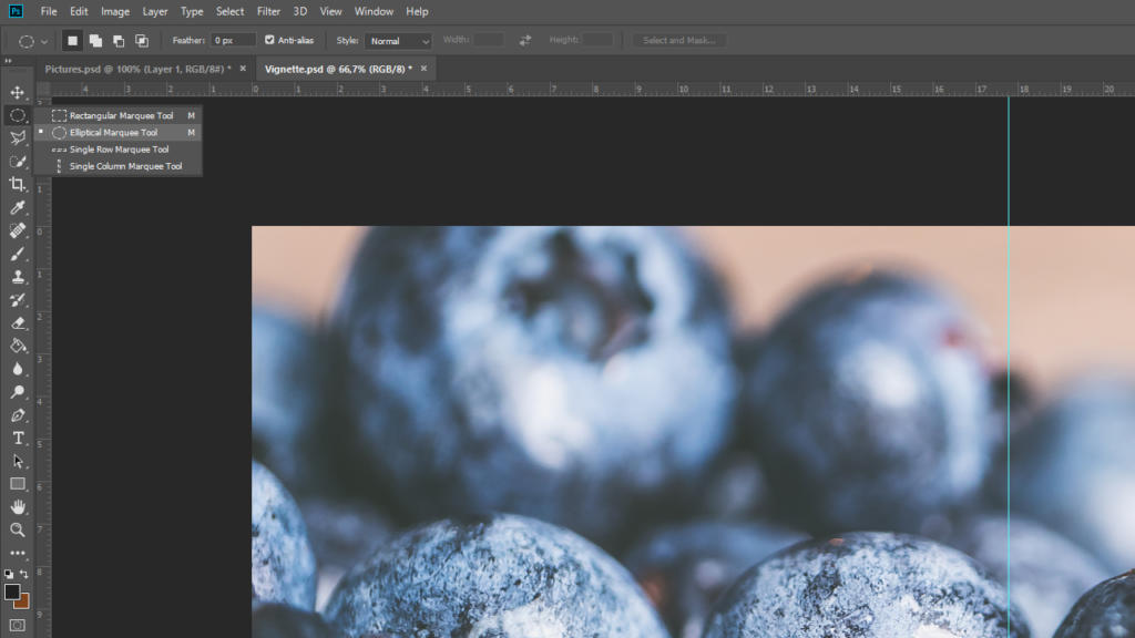 Primo piano di uno schermo di computer che mostra un software di editing delle immagini con una foto di mirtilli. Lo strumento Rectangle Marquee Tool è selezionato sulla barra degli strumenti di sinistra e diverse opzioni di strumenti, tra cui Vignettatura in Photoshop, sono visibili in un menu a discesa.
