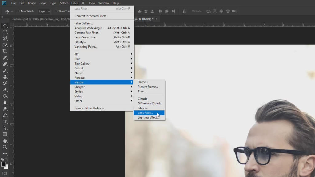 Uno schermo di computer mostra Photoshop con il menu Filtro aperto, che mostra le opzioni Render. Effetto riflesso lente esalta la scena mentre una persona con gli occhiali appare nell'angolo in basso a destra. Lo sfondo è artisticamente sfocato.