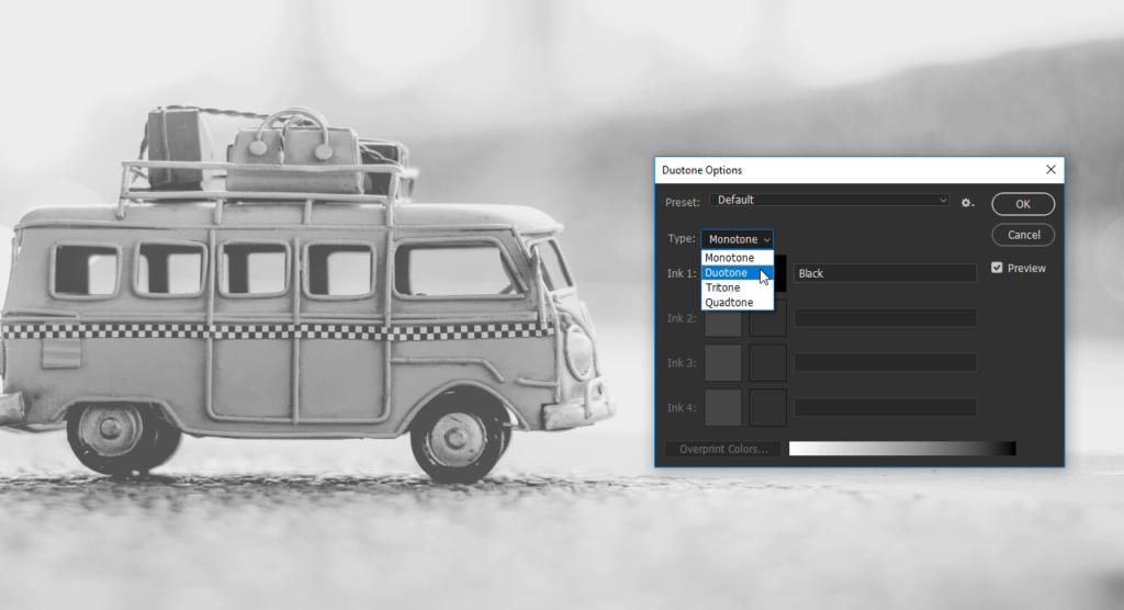 Una foto in bianco e nero di un autobus giocattolo d'epoca con un bagaglio sopra è appoggiata su una superficie piana. Una finestra software aperta con opzioni come "effetto seppia" sovrappone l'immagine, visualizzando un menu a discesa con Duotone selezionato.