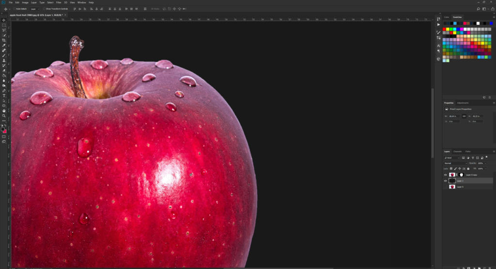 Primo piano di una mela rossa con gocce d'acqua, visualizzata in Photoshop. Il lato sinistro risalta su uno sfondo nero, mentre quello destro mostra l'interfaccia e gli strumenti di Photoshop. Perfetto per dimostrare come attenuare i bordi con Photoshop per una finitura morbida e raffinata.