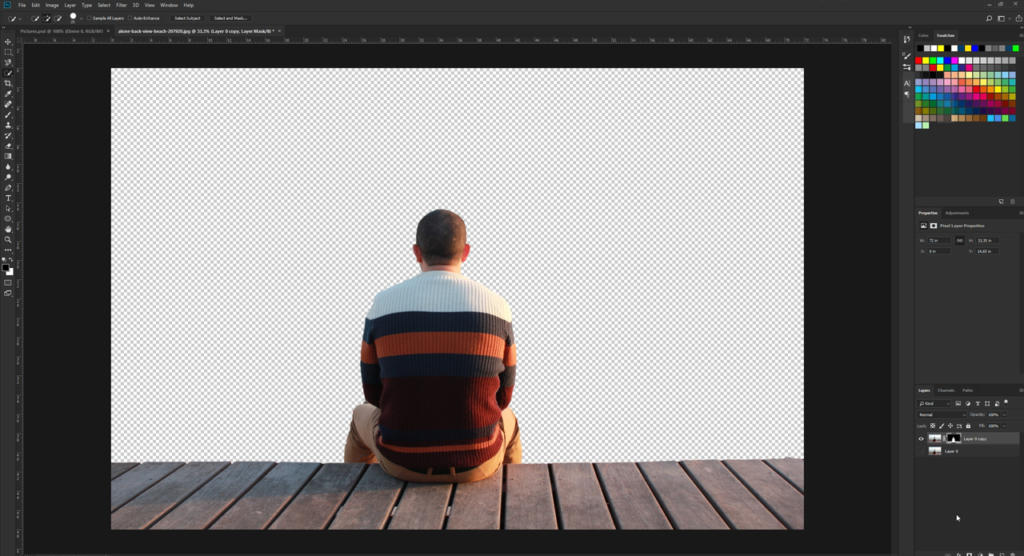 Una persona con un maglione a righe è seduta su un ponte di legno, vista da dietro in uno spazio di lavoro di editing digitale. Lo sfondo trasparente mostra la sfocatura e le palette di colori all'interno di Photoshop, con vari strumenti di editing sparsi nell'immagine.