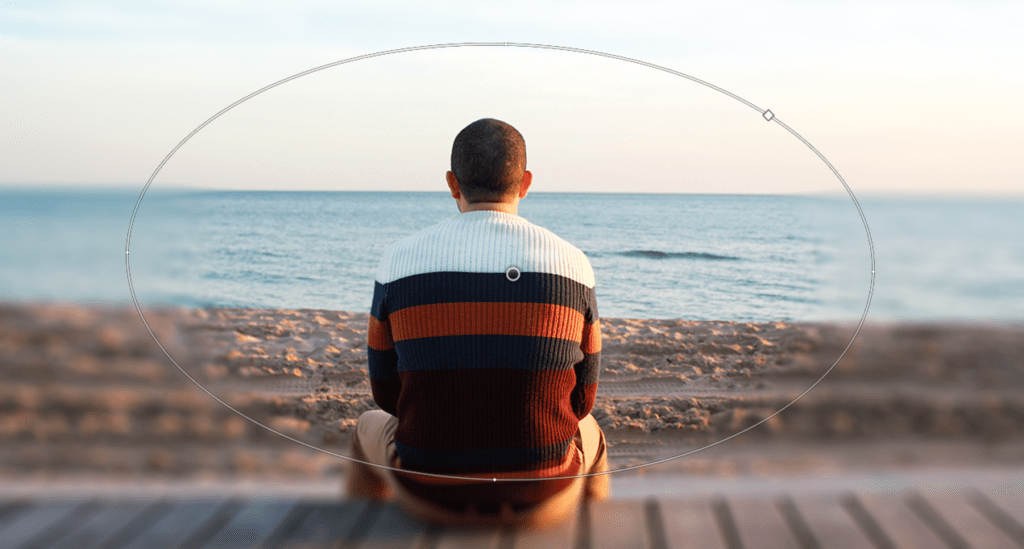 Una persona siede su una panchina di legno di fronte all'oceano, indossando un maglione a righe nei toni del blu, bianco e arancione. Il cielo e il mare si fondono senza soluzione di continuità in un sereno effetto sfocatura, evocando tranquillità in questa scena pittoresca.