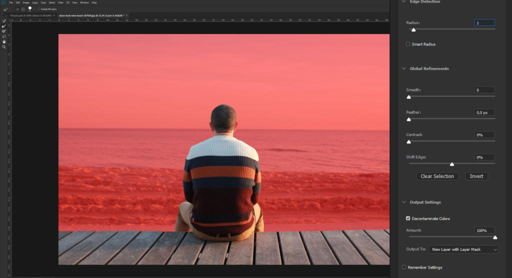 Una persona con i capelli corti e un maglione a righe multicolori è seduta su un ponte di legno, di fronte a un oceano dalle sfumature rosse. L'immagine, con effetti di sfocatura, è aperta in Photoshop con strumenti e impostazioni di regolazione sul lato destro.