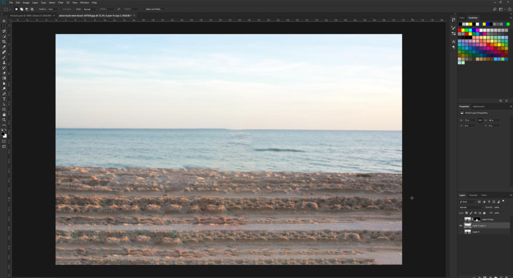 Un'interfaccia di editing di immagini digitali mostra una scena di spiaggia serena, evocando la calma di un oceano tranquillo con onde dolci e una spiaggia sabbiosa. Vari strumenti di editing, tra cui l'opzione sfocatura in Photoshop e palette di colori vivaci, circondano il bordo dello schermo.