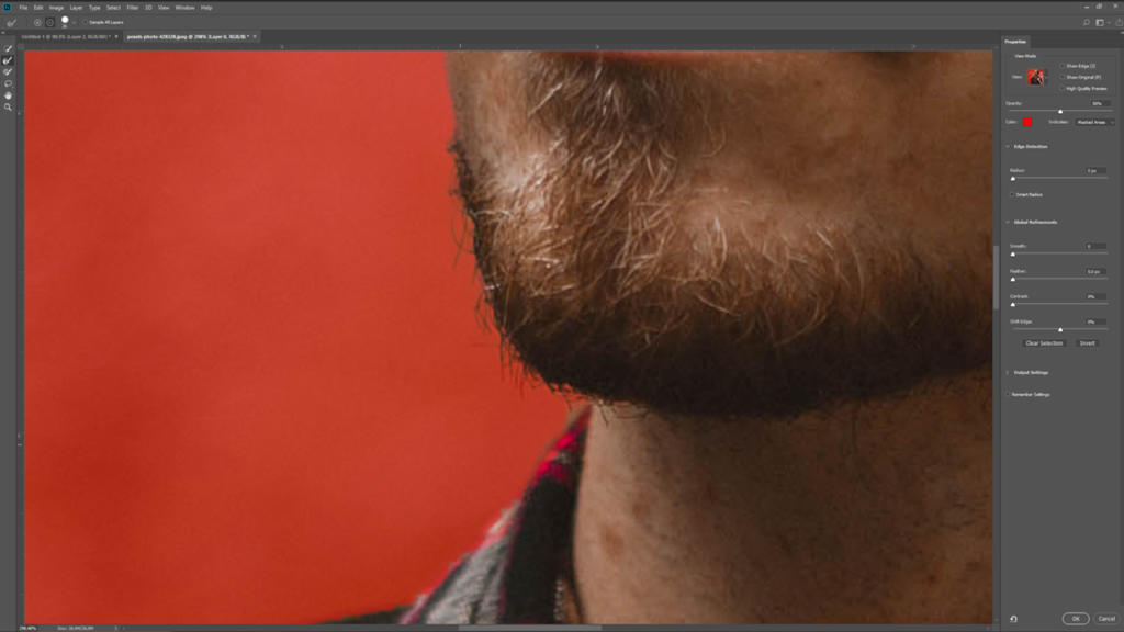 Primo piano del mento di una persona con la barba visualizzato sullo schermo di un computer, pronto per essere ritagliato in Photoshop. Lo sfondo è di un rosso acceso e gli strumenti di modifica sono visibili sul lato destro dello schermo.