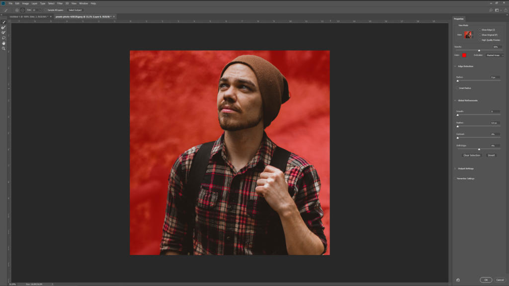 Un uomo con un berretto marrone e una camicia a quadri guarda pensieroso verso l'alto contro uno sfondo rosso acceso. L'immagine, che viene ritagliata in Photoshop, mostra le opzioni di regolazione sul lato destro del software di editing.