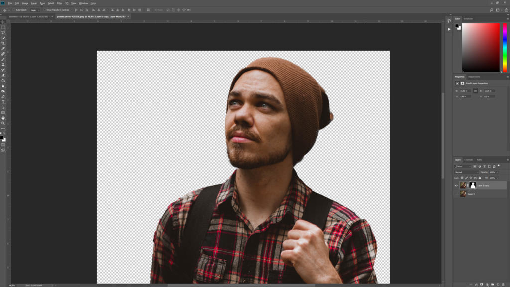 Una persona con la barba, che indossa un berretto marrone e una camicia a quadri, è in piedi su uno sfondo trasparente, come se fosse stata ritagliata con Photoshop, e guarda verso l'alto con aria pensierosa.
