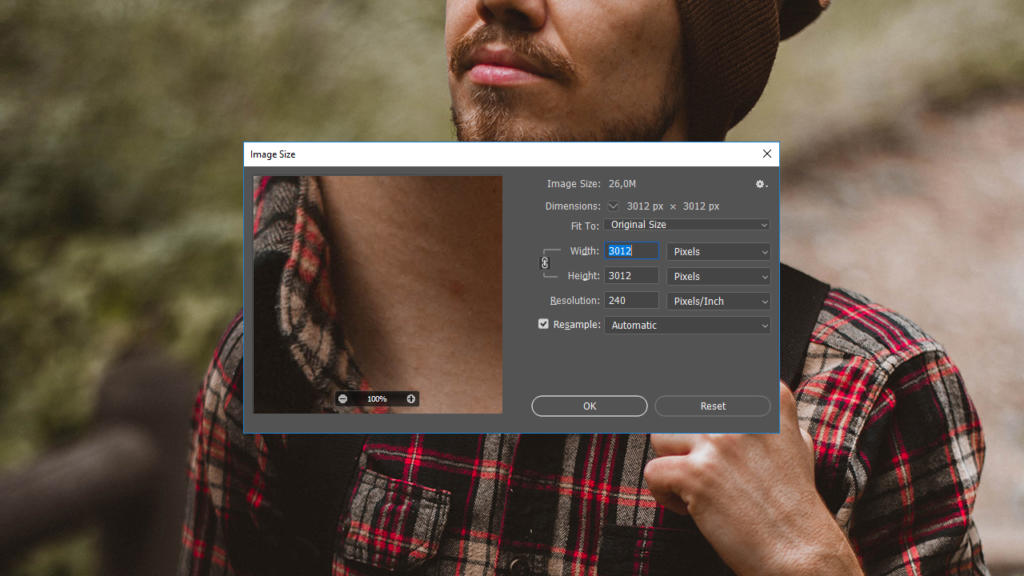 Una persona con una camicia a quadri e un cappello marrone è in piedi all'aperto contro uno sfondo naturale sfocato. La finestra del software di modifica delle immagini, che mostra strumenti come "taglia in Photoshop", oscura parzialmente il suo petto, rivelando le dimensioni e i dettagli dell'immagine.