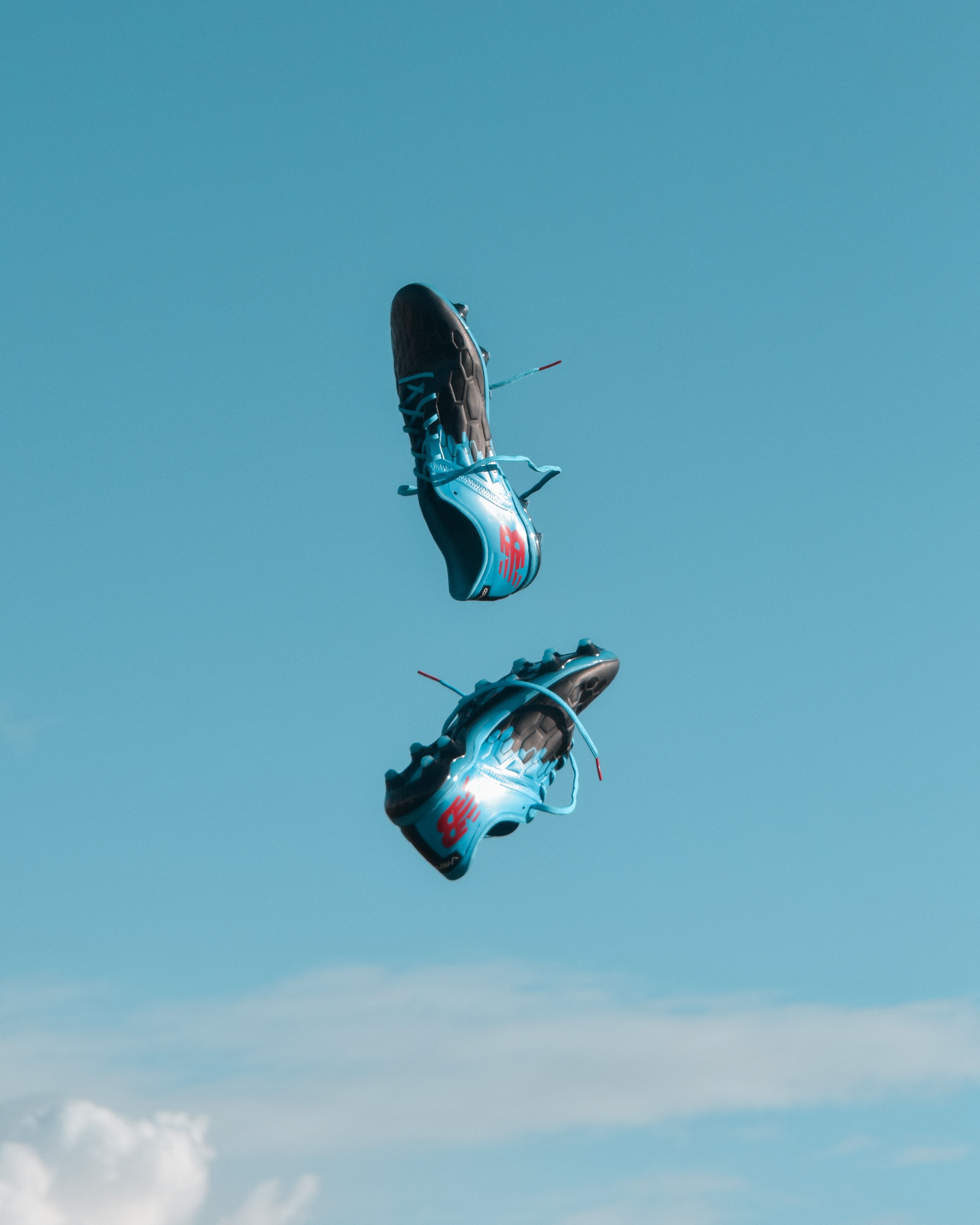 Due sneaker blu con accenti rossi si librano in un cielo limpido, ricordando le emozionanti giocate degli Europei del 2021. La loro danza a mezz'aria contro nuvole vaporose incarna movimento dinamico e libertà, catturando un momento di pura esaltazione.