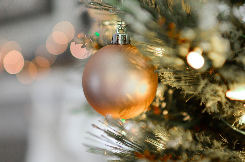 Un primo piano di un ornamento in vetro smerigliato appeso a un albero di Natale. L'ornamento riflette luci soffuse e calde e luci bokeh sfocate sono visibili sullo sfondo, creando un'atmosfera accogliente e festosa.