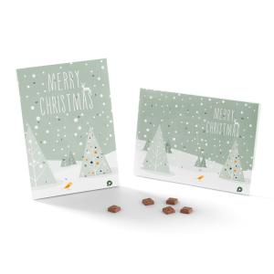 Due biglietti di Natale con un disegno di un albero innevato e testo Merry Christmas su uno sfondo verde chiaro. Cinque piccoli dolcetti marroni sono posizionati davanti ai biglietti.
